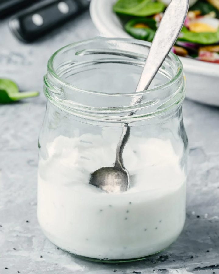Transparent jar with bleu cheese dressing and a metal spoon.