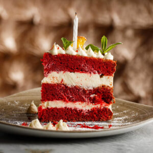 Close look of a slice of red velvet cake with a birthday candle.