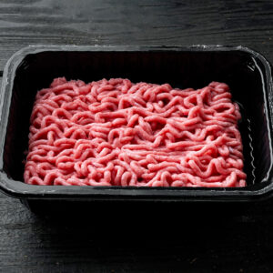 Plastic container with thawed mince sitting on a dark table.