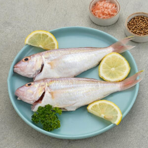 Two cleaned croaker fishes on a blue plate with lemon slices, black pepper and salt.