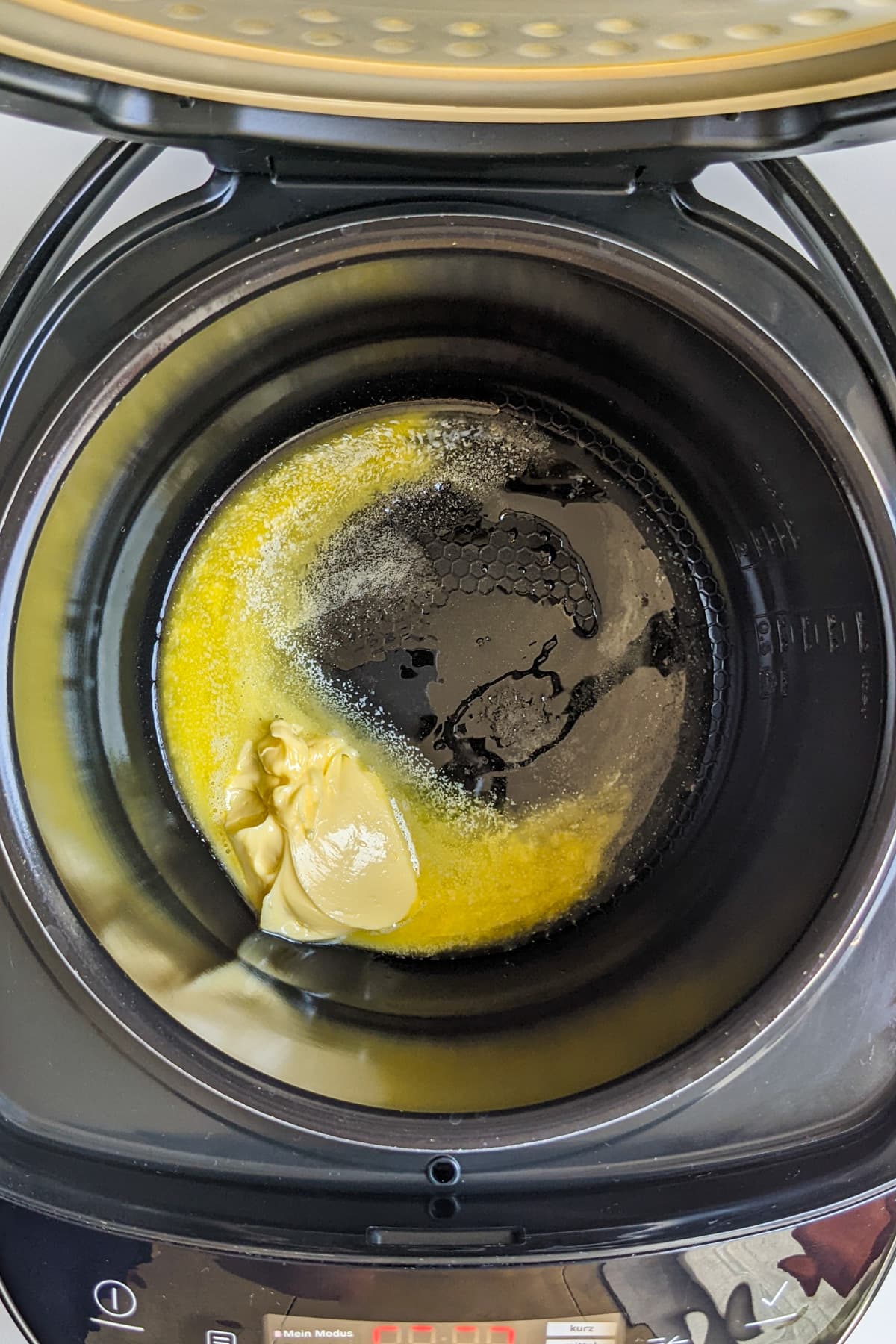 Top view of a slow cooker with a piece of butter and olive oil inside of it.