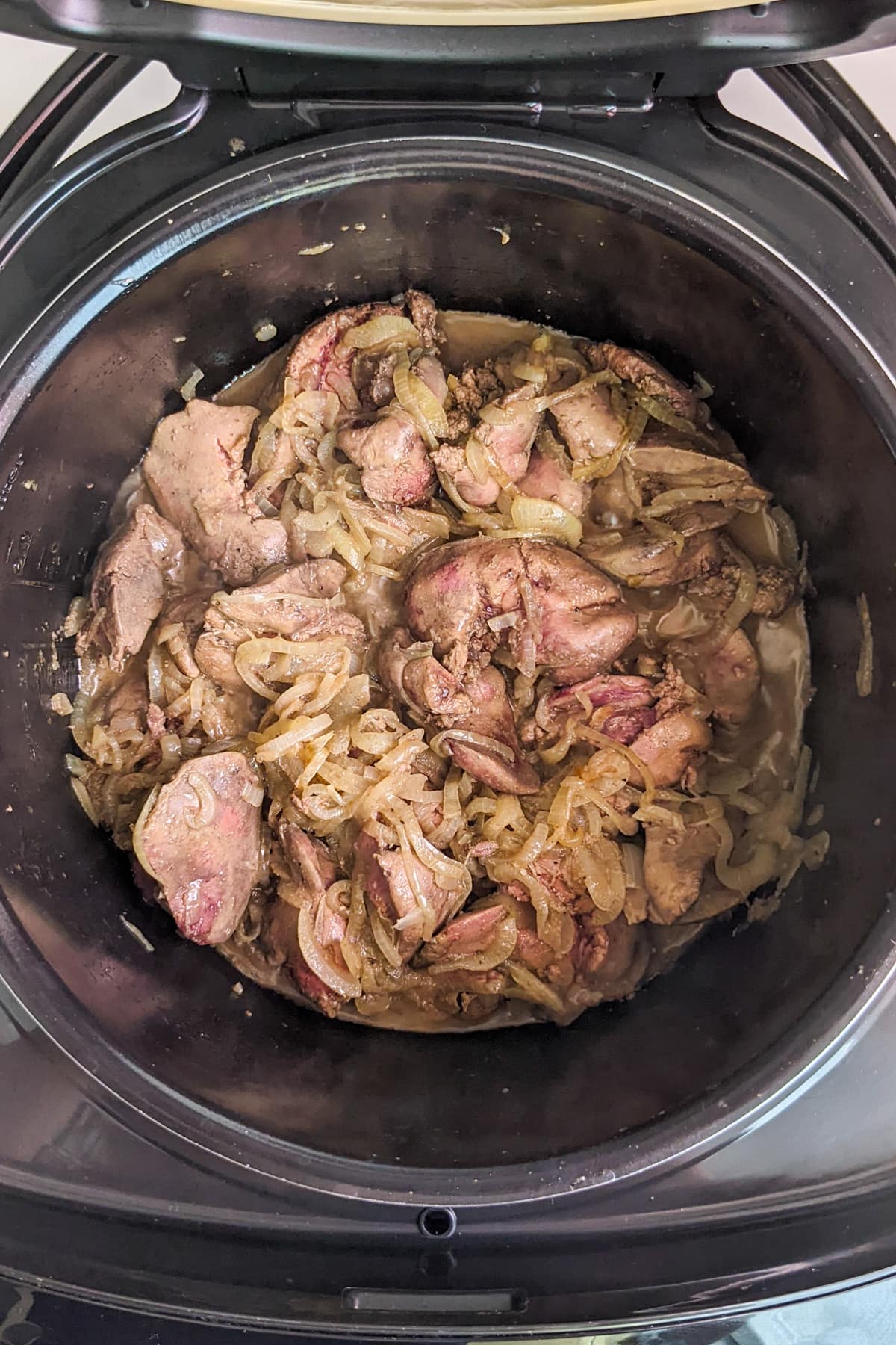 Top view of slow cooker with liver and onions simmering inside.