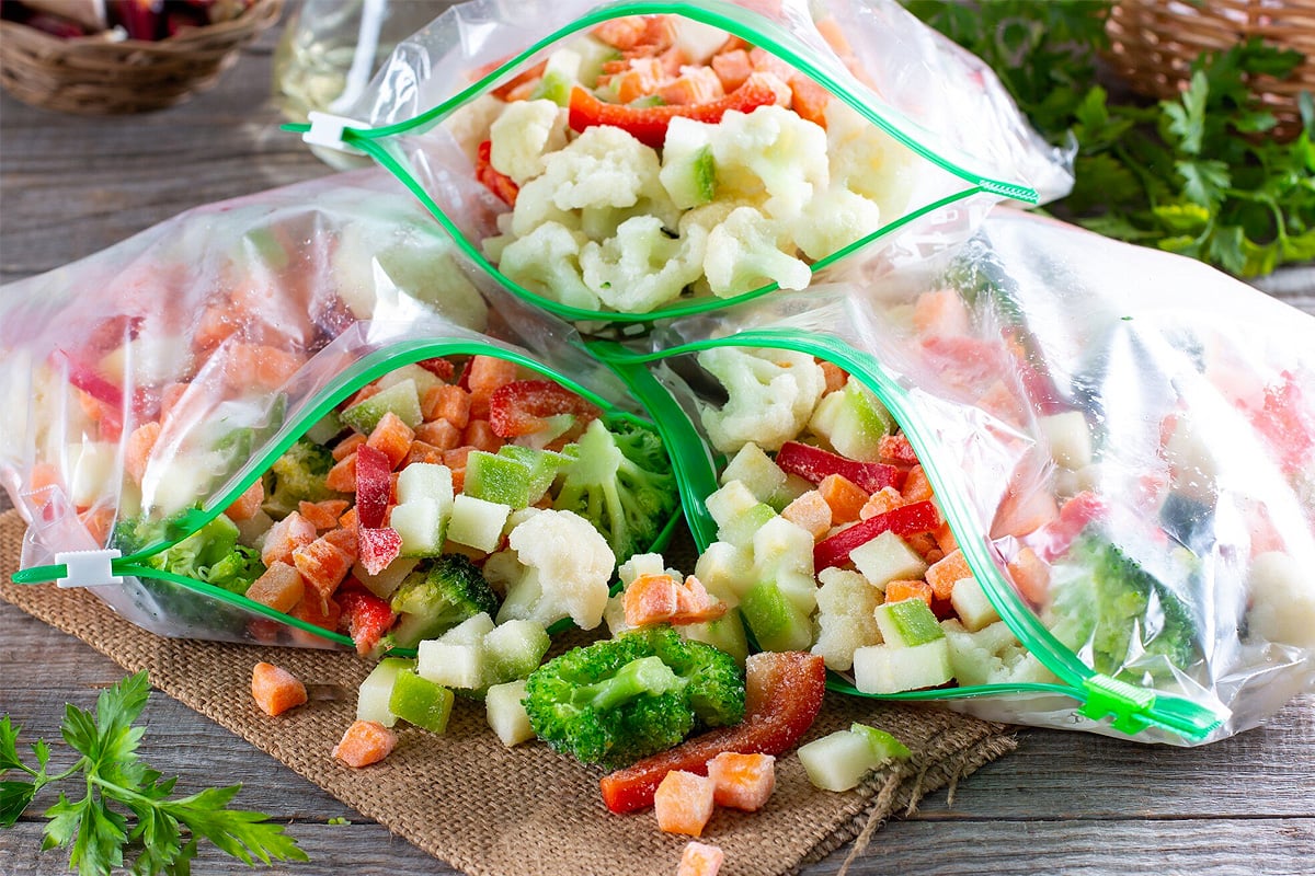 3 opened freezing bag with frozen pieces of vegetables on a wooden table.
