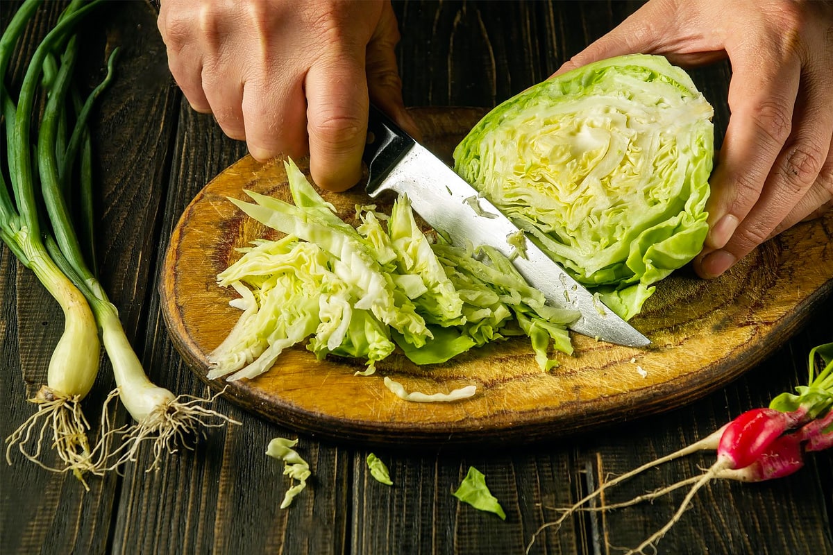 Two hands with a knife cutting lettuce.