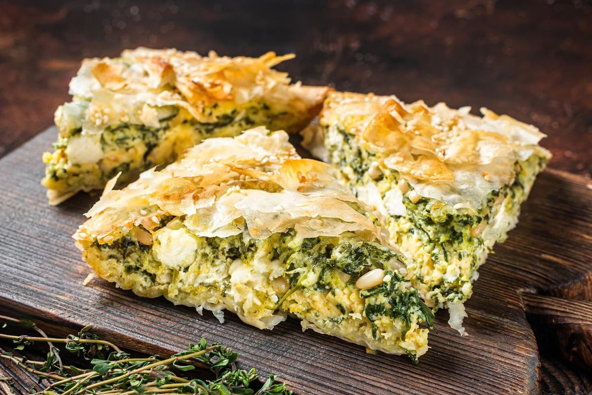 3 slices of spanakopita on a wooden board.