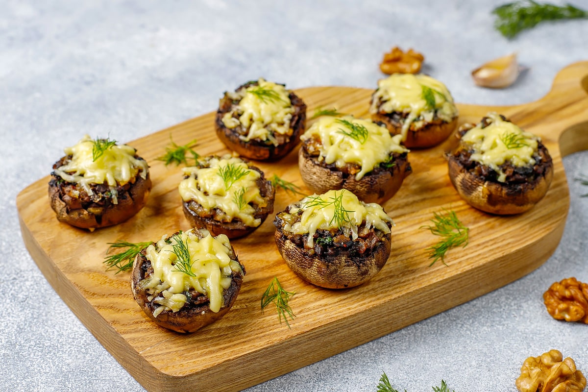 Wooden board with 8 stuffed mushrooms with cheese.
