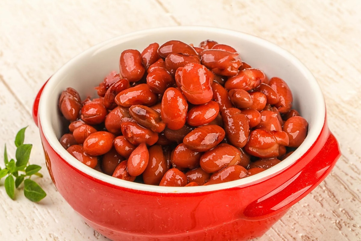 Cooked pinto beans in a red bowl on a wooden table.