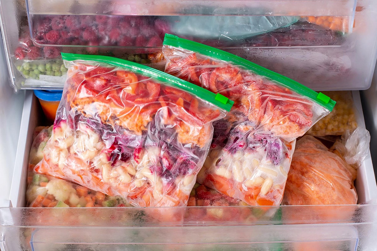 Two freezing bags with cooked vegetables sitting in an opened freezer drawer..