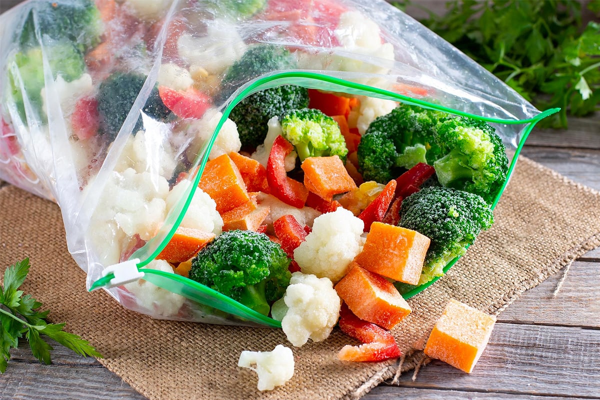 Opened freezing bag with frozen pieces of vegetables on a wooden table.