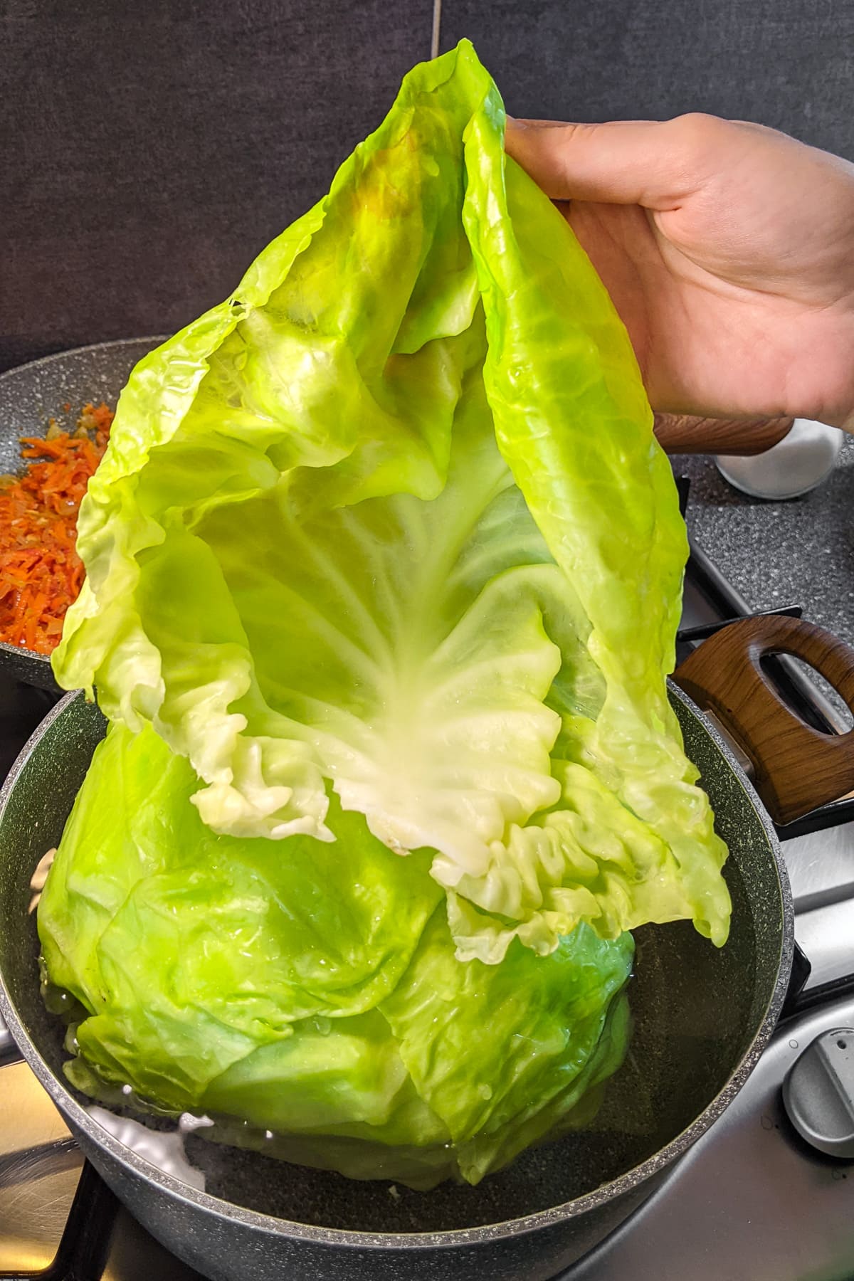 Woman hand holding a cabbage leaf over a pan with boiled water.
