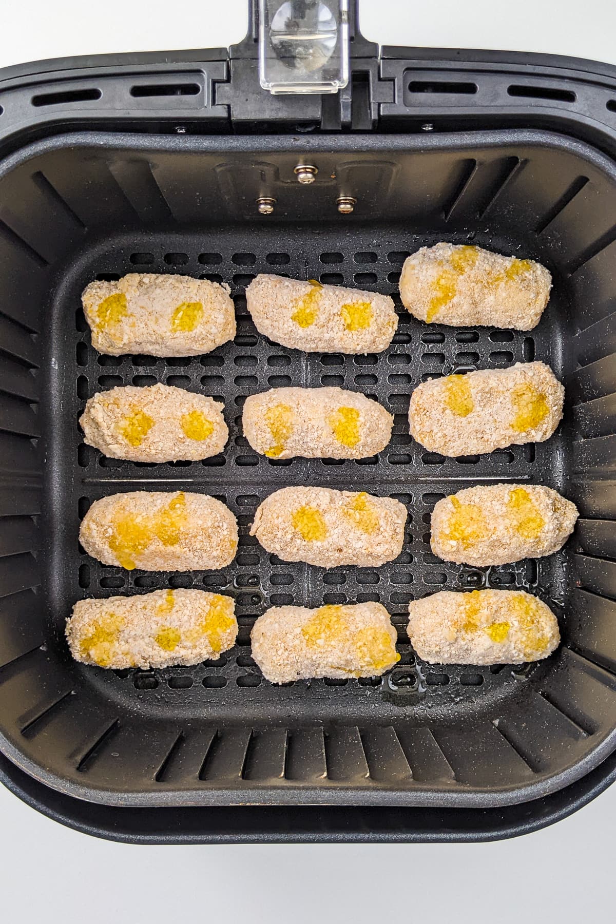 Top view of raw chili cheese nuggets in an air fryer basket.