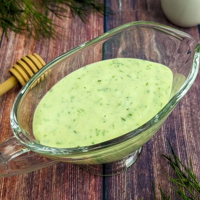 Close look of glass full of honey dill sauce with some dill leaves.