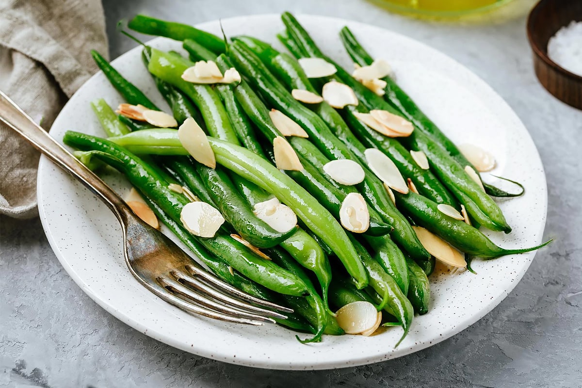 Close look of green beans with almonds on a white plate with a fork near.