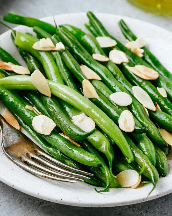 Close look of green beans with almonds on a white plate with a fork near.
