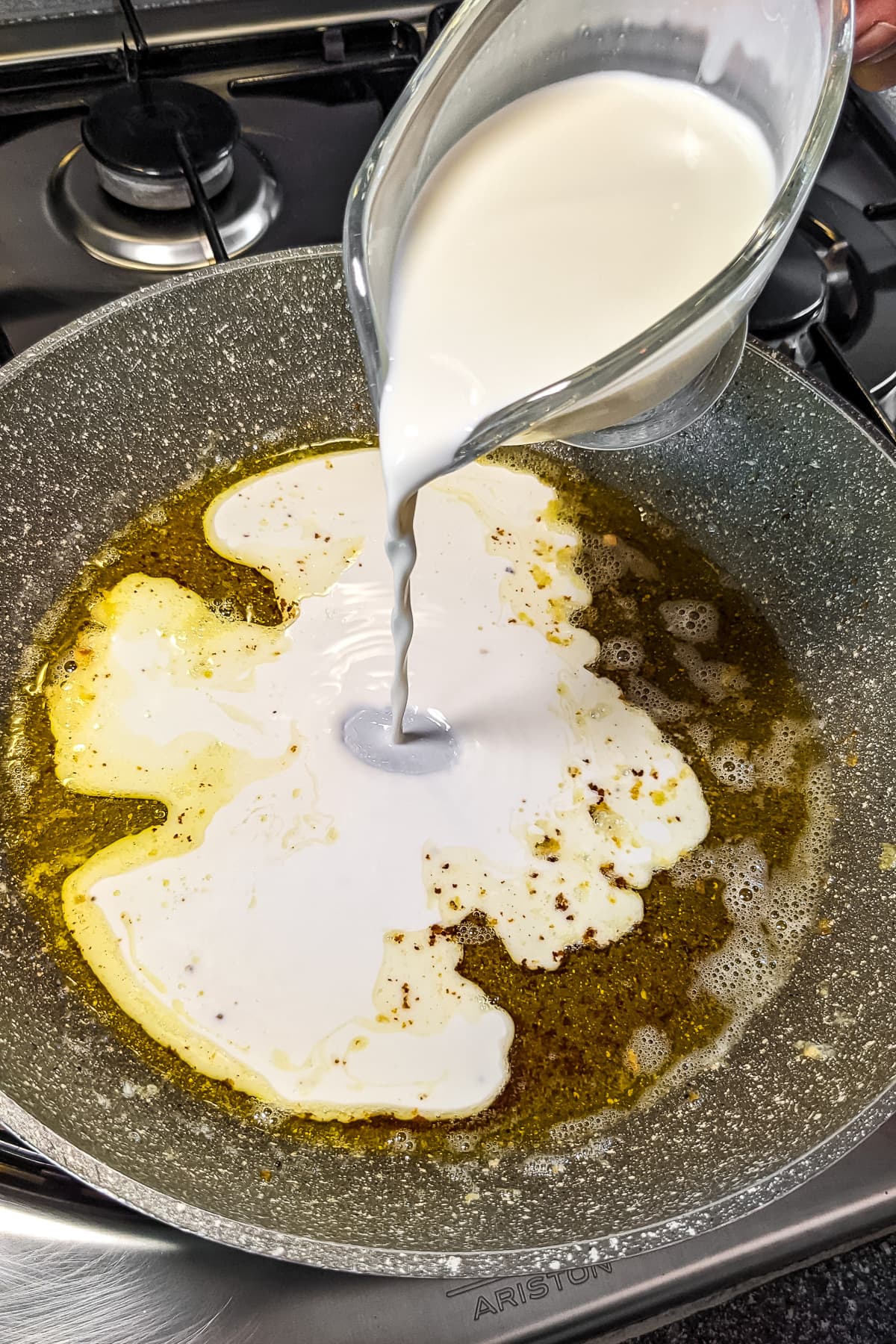 Pouring half and half over the melted butter in a sauce pan.