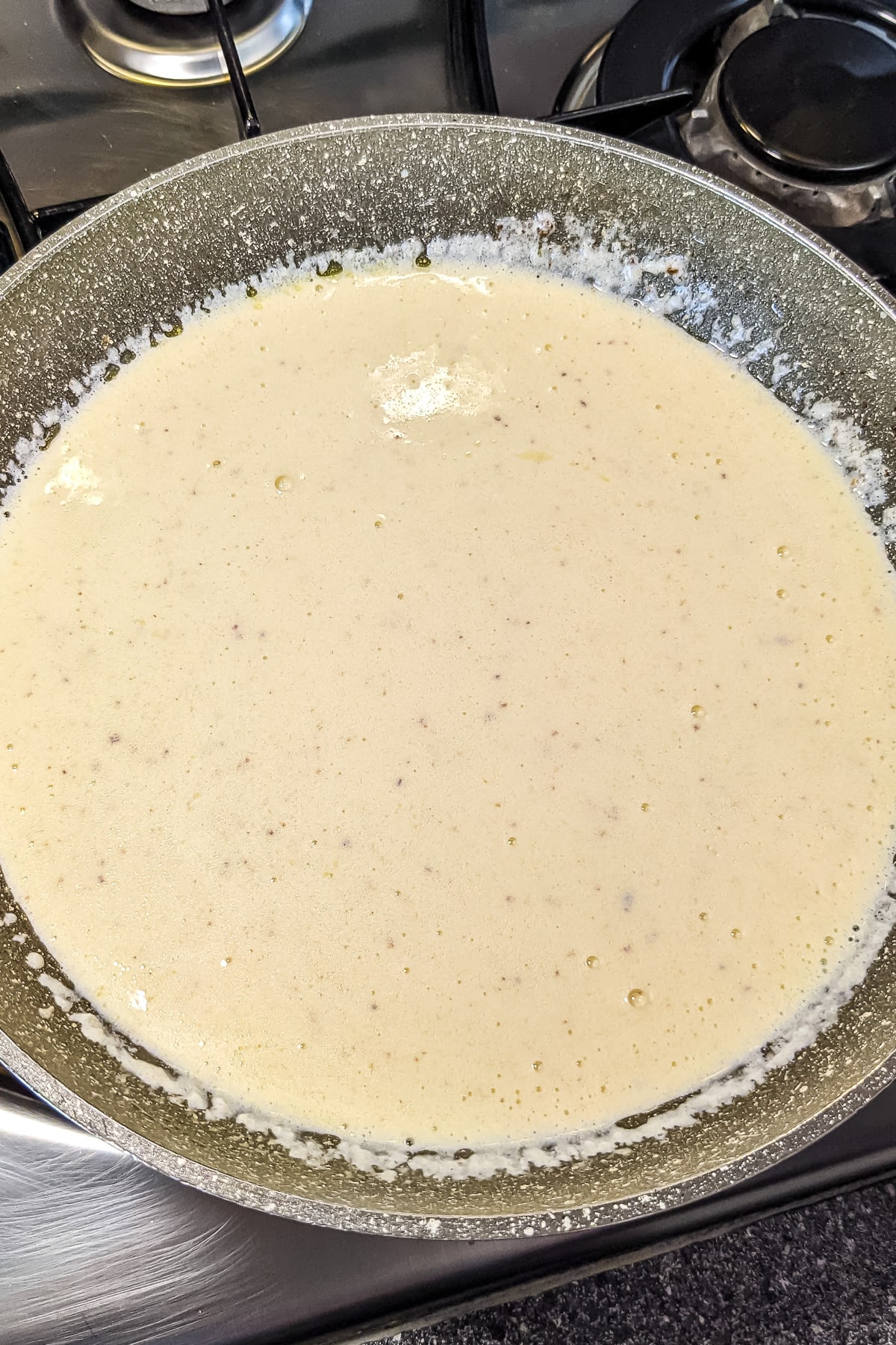 Top view of a sauce pan with cooked alfredo sauce with half and half.