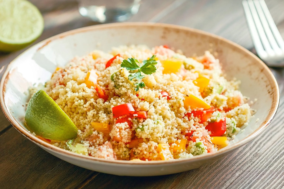 Cooked couscous with fresh vegetables and lime slice.