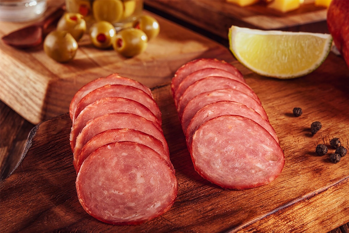 Close look of sliced summer sausage on a wooden board with lemon and olives.