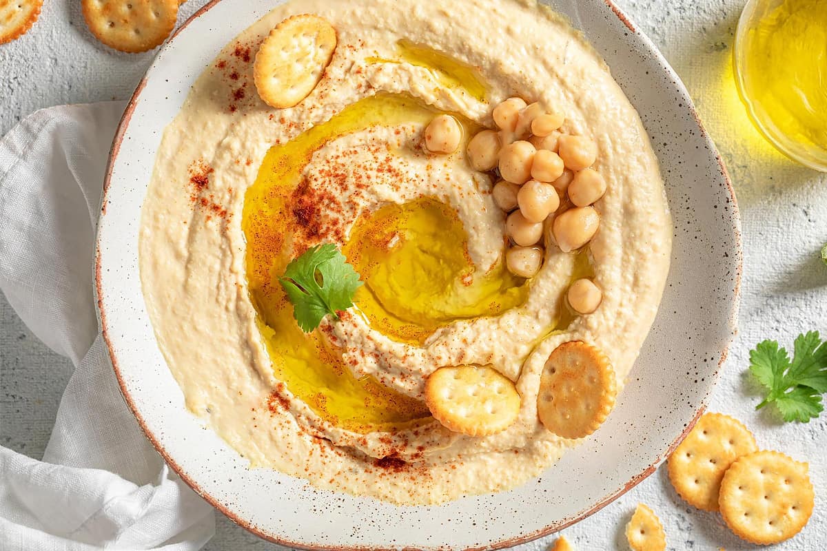 Top view of chickpea hummus with nuts and biscuits.