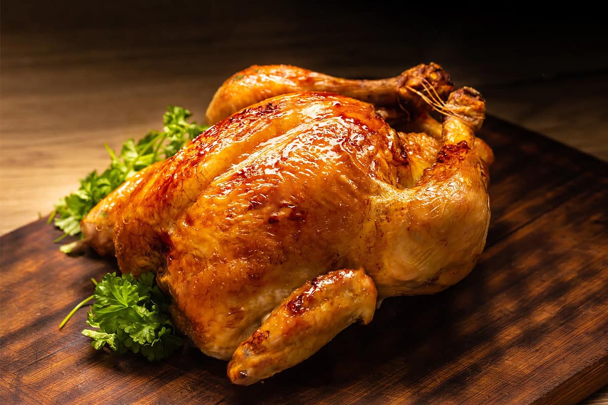 Close look of a whole roasted chicken on a wooden cutting board.
