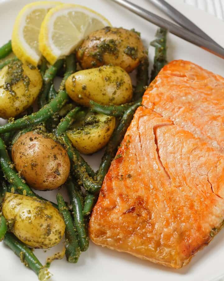 Close look of a piece of salmon served near roasted potatoes with green beans and lemon slices.