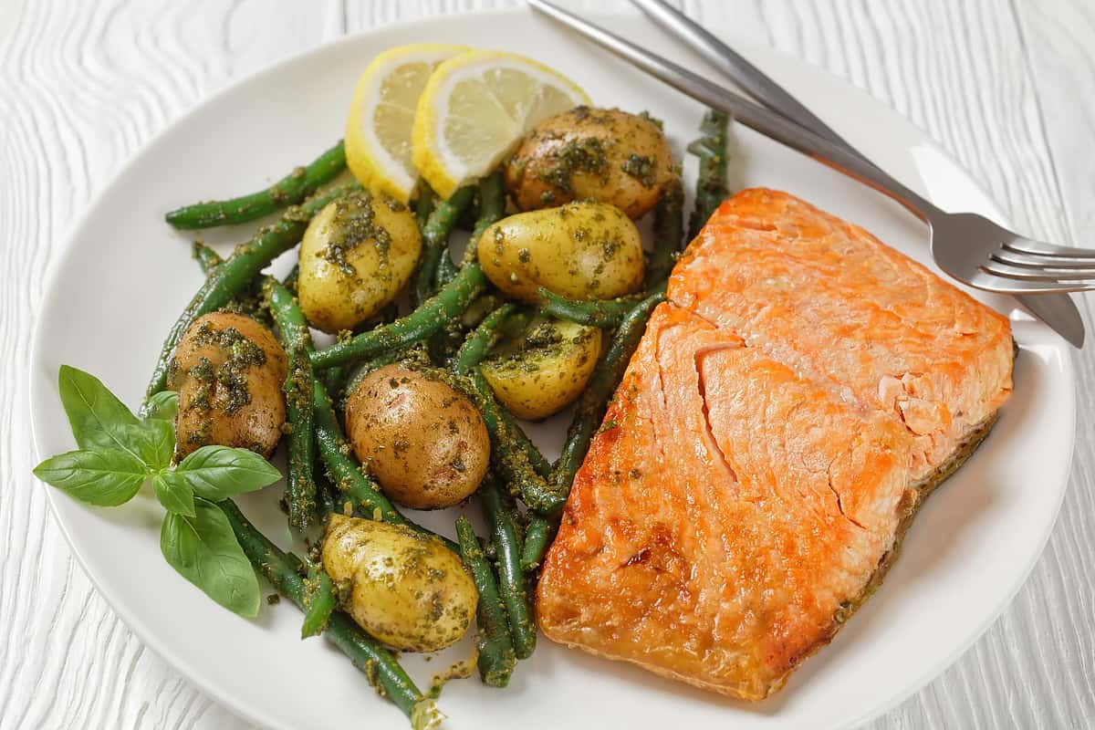Close look of a piece of salmon served near roasted potatoes with green beans and lemon slices.