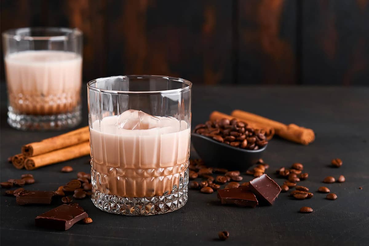 Close look of a glass with Irish cream and ice cube with coffee and chocolate.