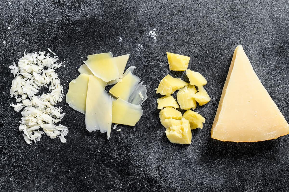 Different forms of parmesan cheese on a black table.