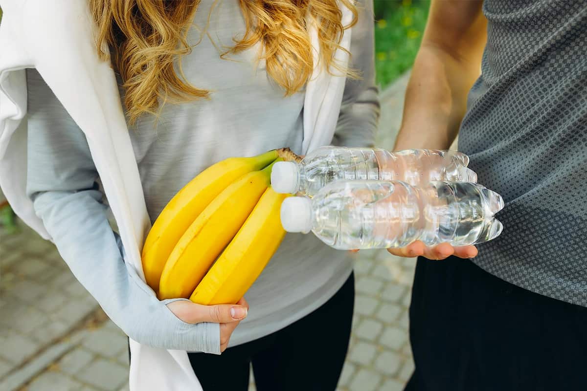 Woman holding 3 bananas and a man holding two bottles of water.