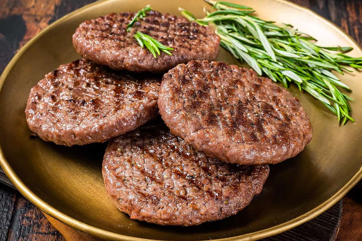 Close look of 4 burger patties with a rosemary branch in a golden plate.