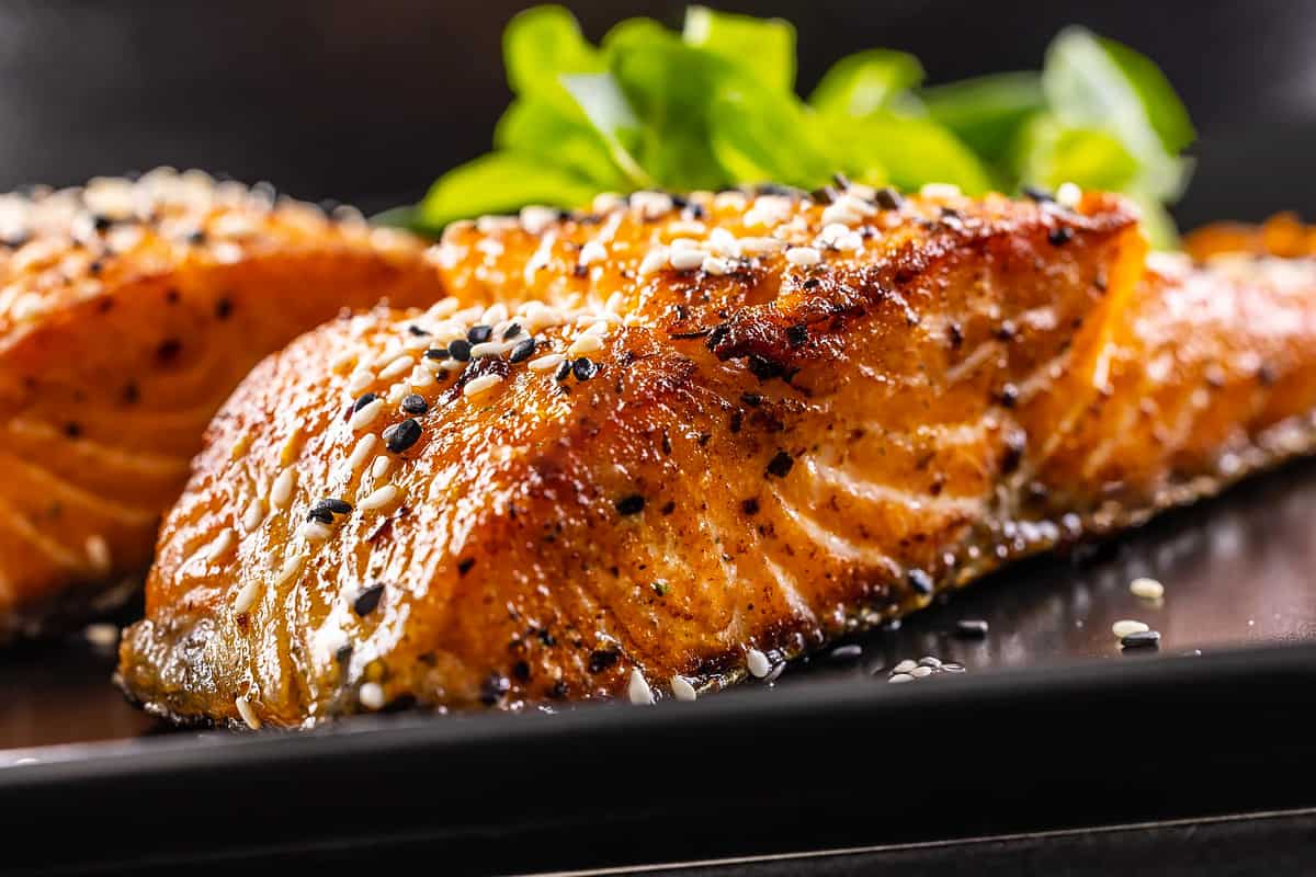 Close look of salmon with sesame seeds on a black plate.