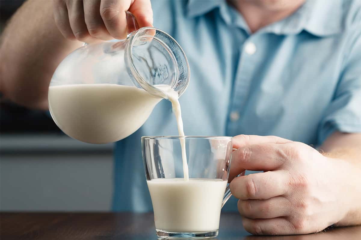 Man hand pouring milk in a transparent glass.