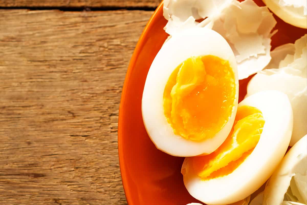Two halves of a boiled eggs in a red plate on a wooden table.