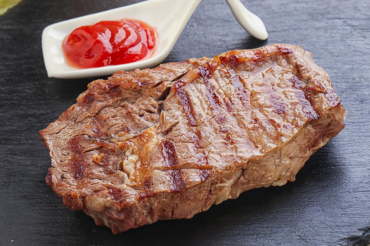 Close look of a beef steak with ketchup on a dark table.