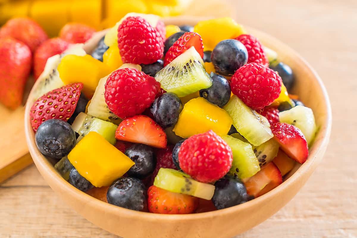 Wooden plate with strawberries, blueberries, kiwi, and mango.