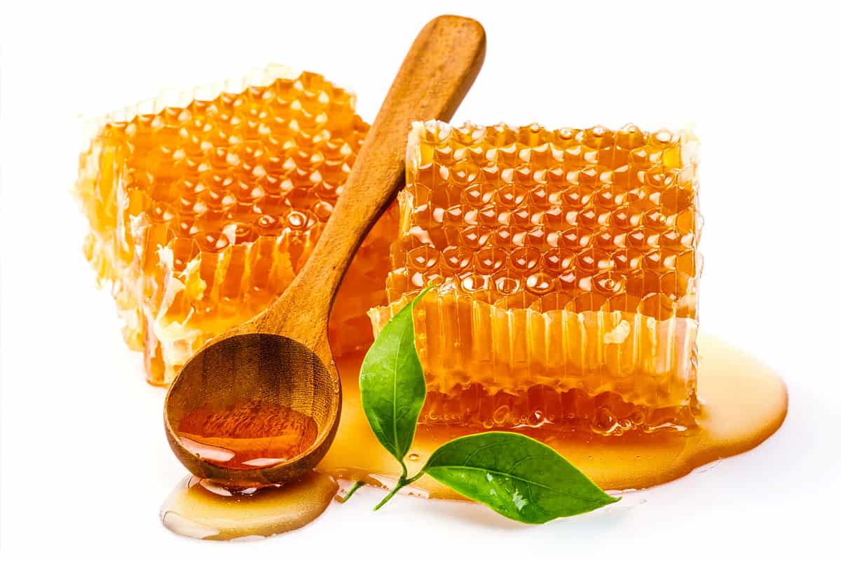 Close look of honeycomb with orange leaves and a wooden spoon.