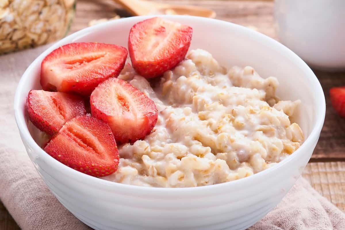White bowl with oatmeal and strawberries halves.