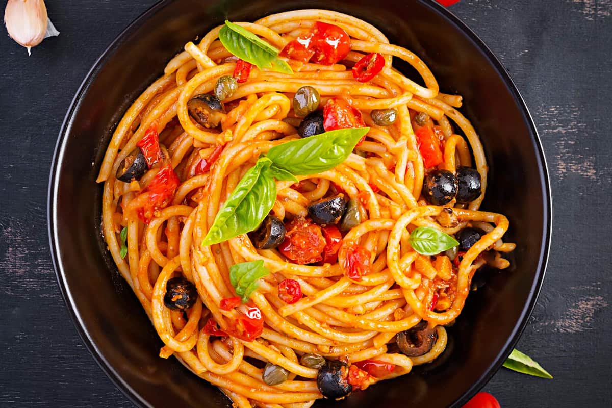 Top view of spaghetti cooked with black olives and tomatoes.