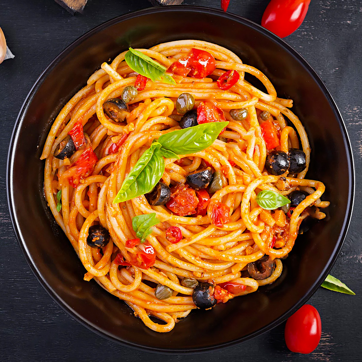 Top view of spaghetti cooked with black olives and tomatoes.