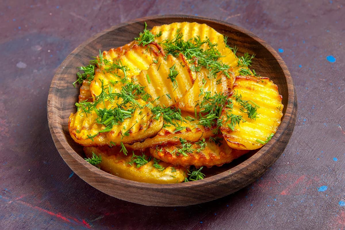 Wooden plate with fried potato slices with chopped dill.