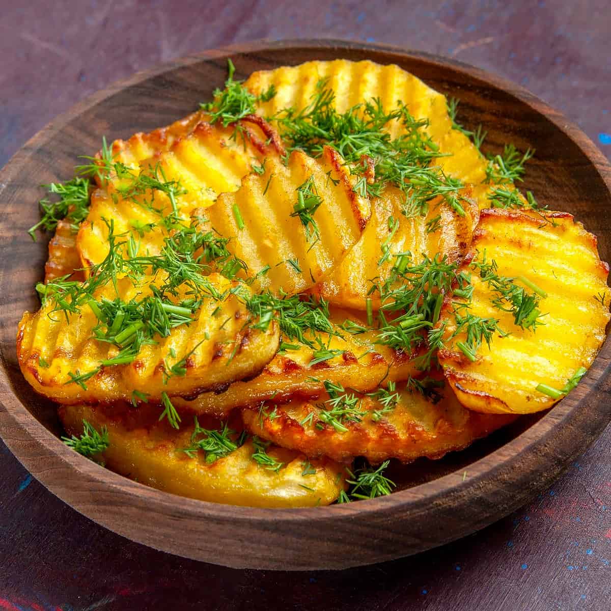 Wooden plate with fried potato slices with chopped dill.