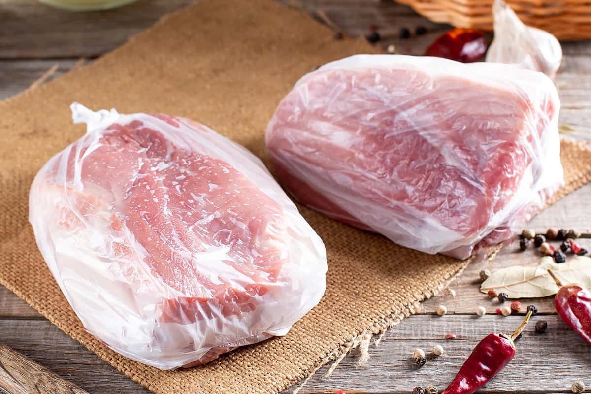 Two bags with frozen pork chops on a wooden table.