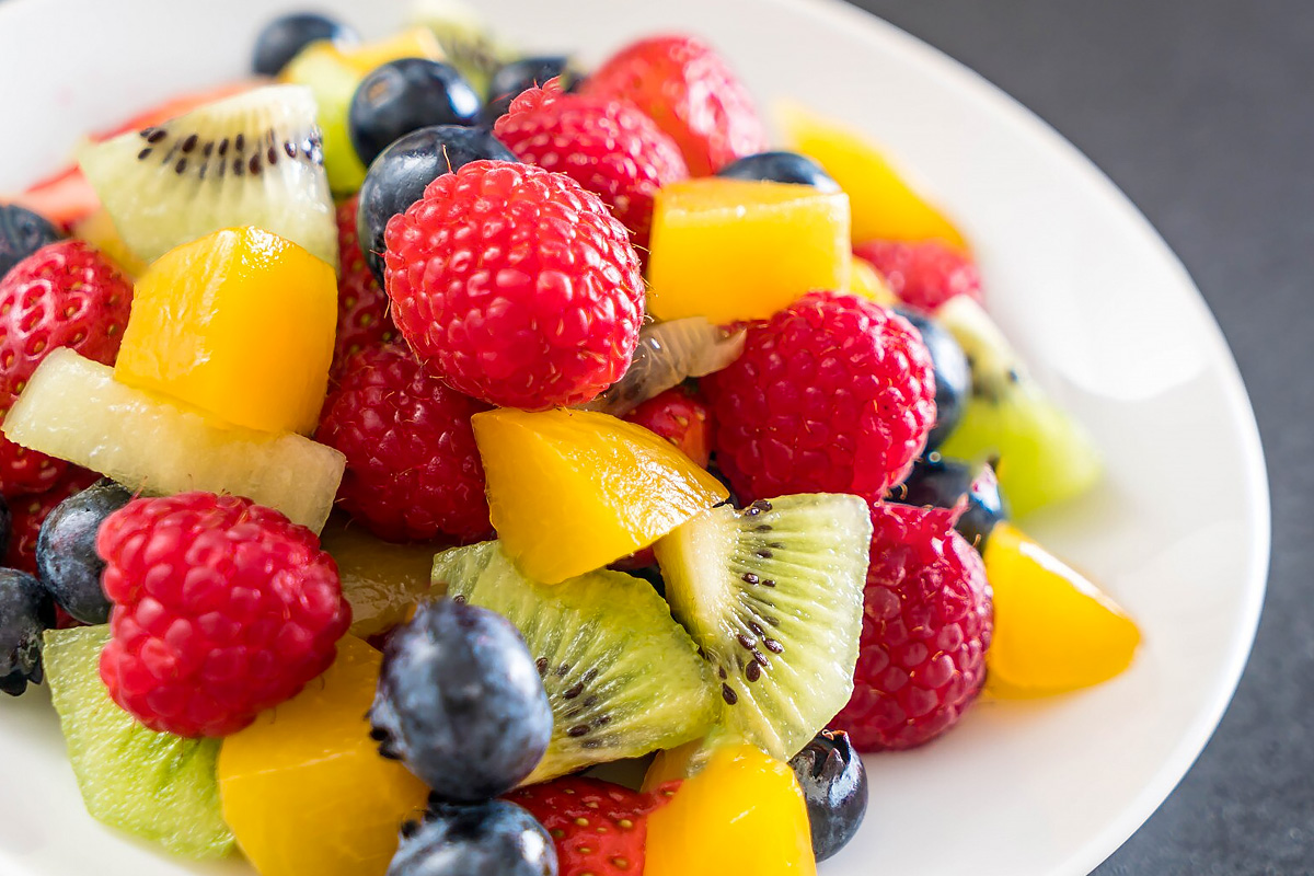 White plate with strawberries, kiwi, mango, and blueberries.