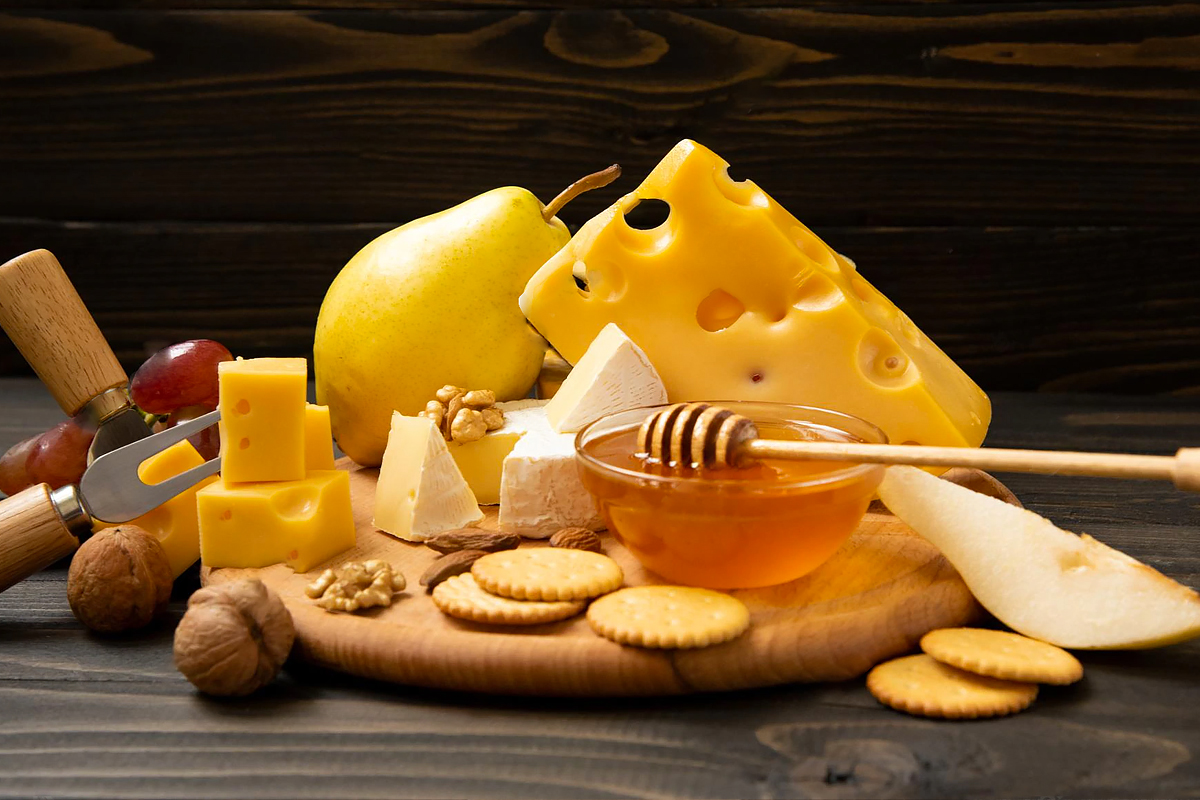 Pear, honey, nuts and a few different types of cheeses on a wooden board.
