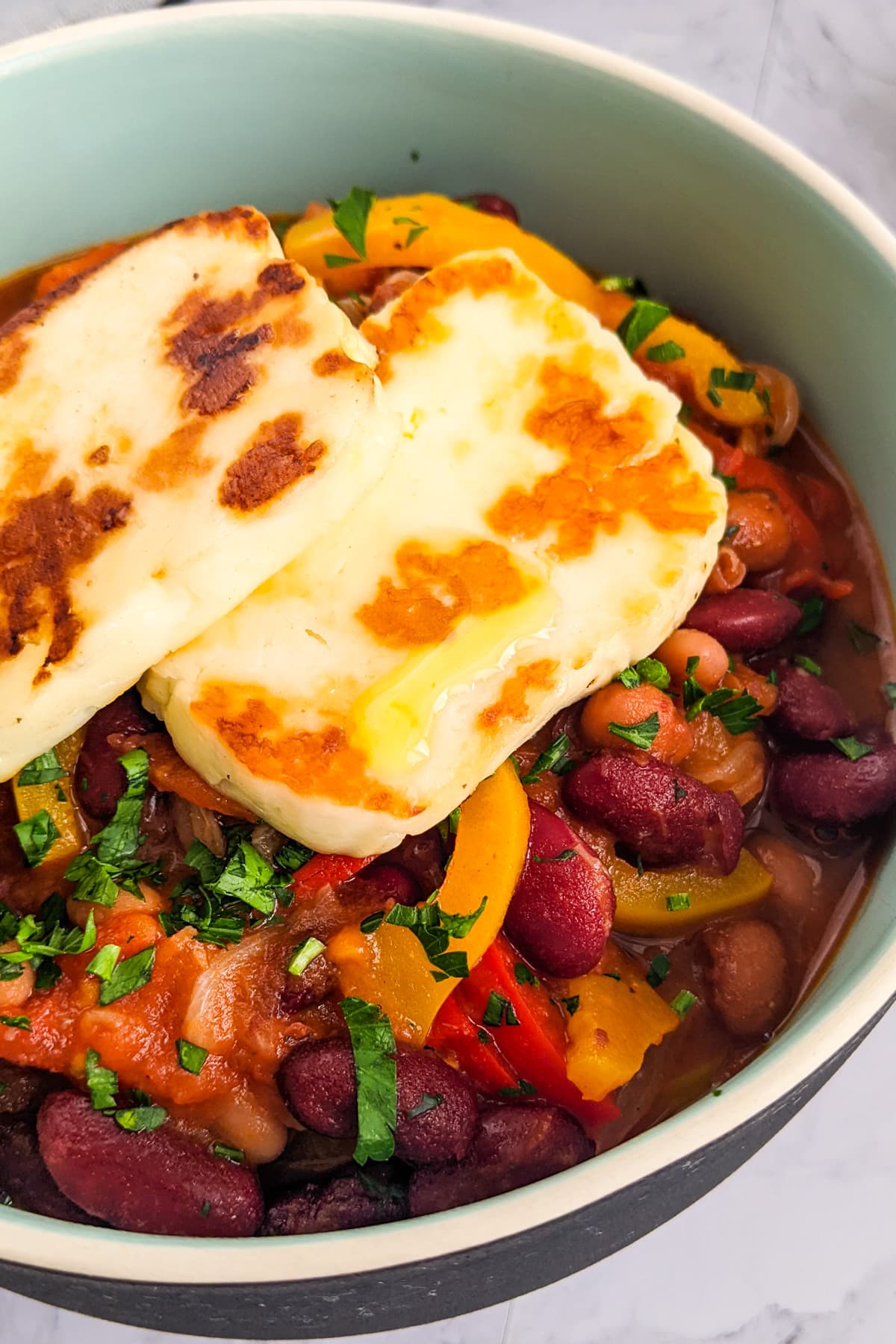Close look of 2 slices of halloumi over a beans stew.