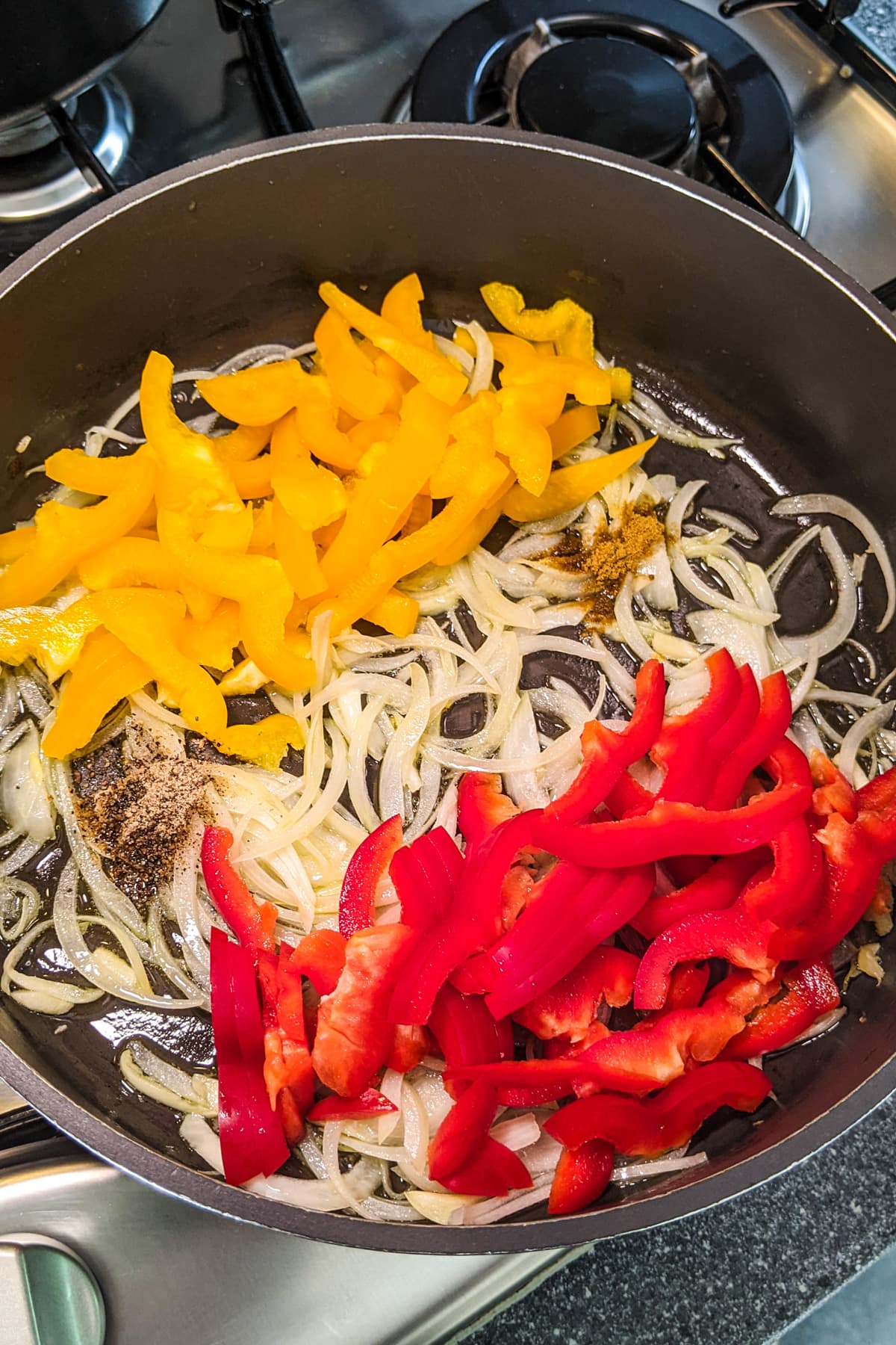 Raw sliced bell peppers over fried onions in a frying pan.
