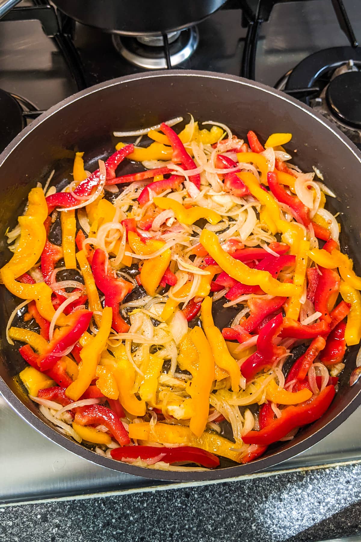 Frying onions with sliced bell peppers on the stove.