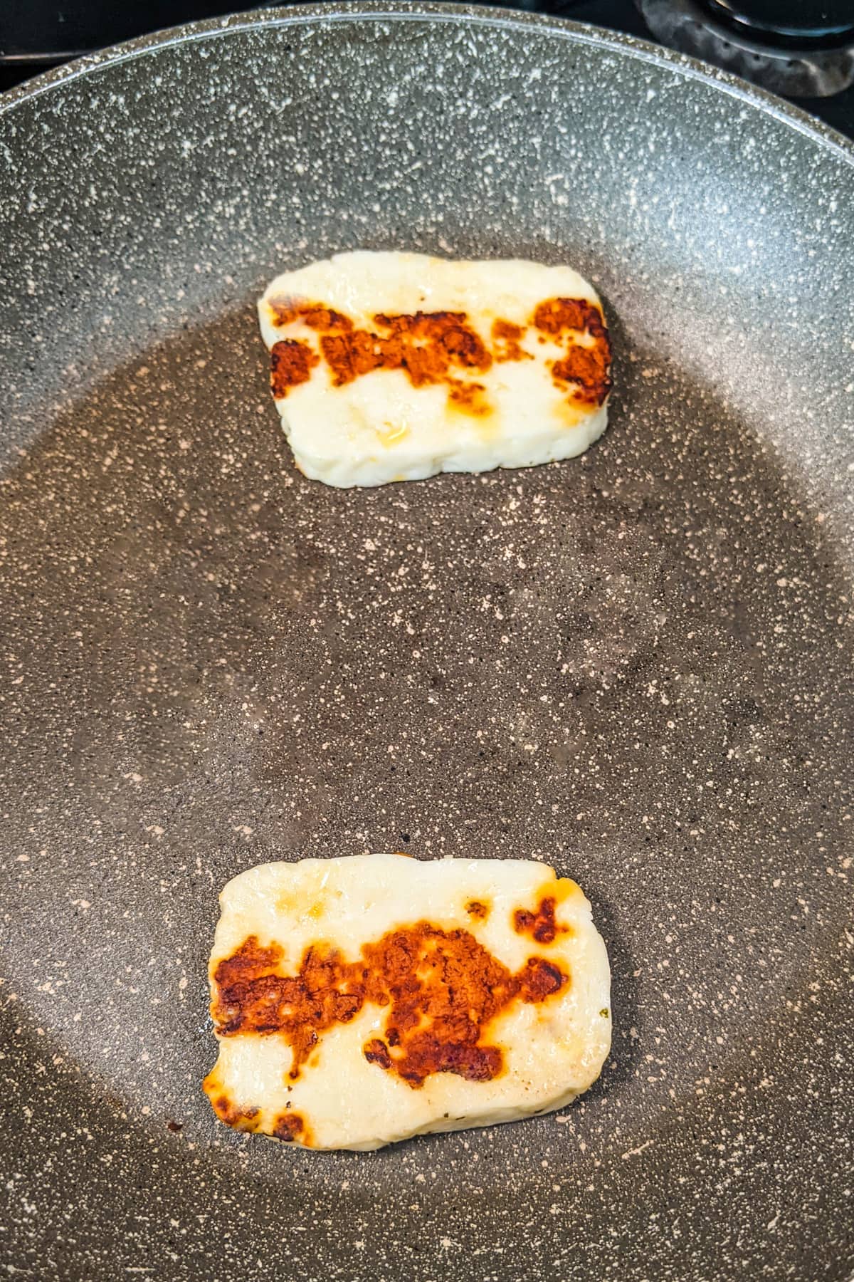 Frying two pieces of halloumi cheese on a frying pan on the stove.