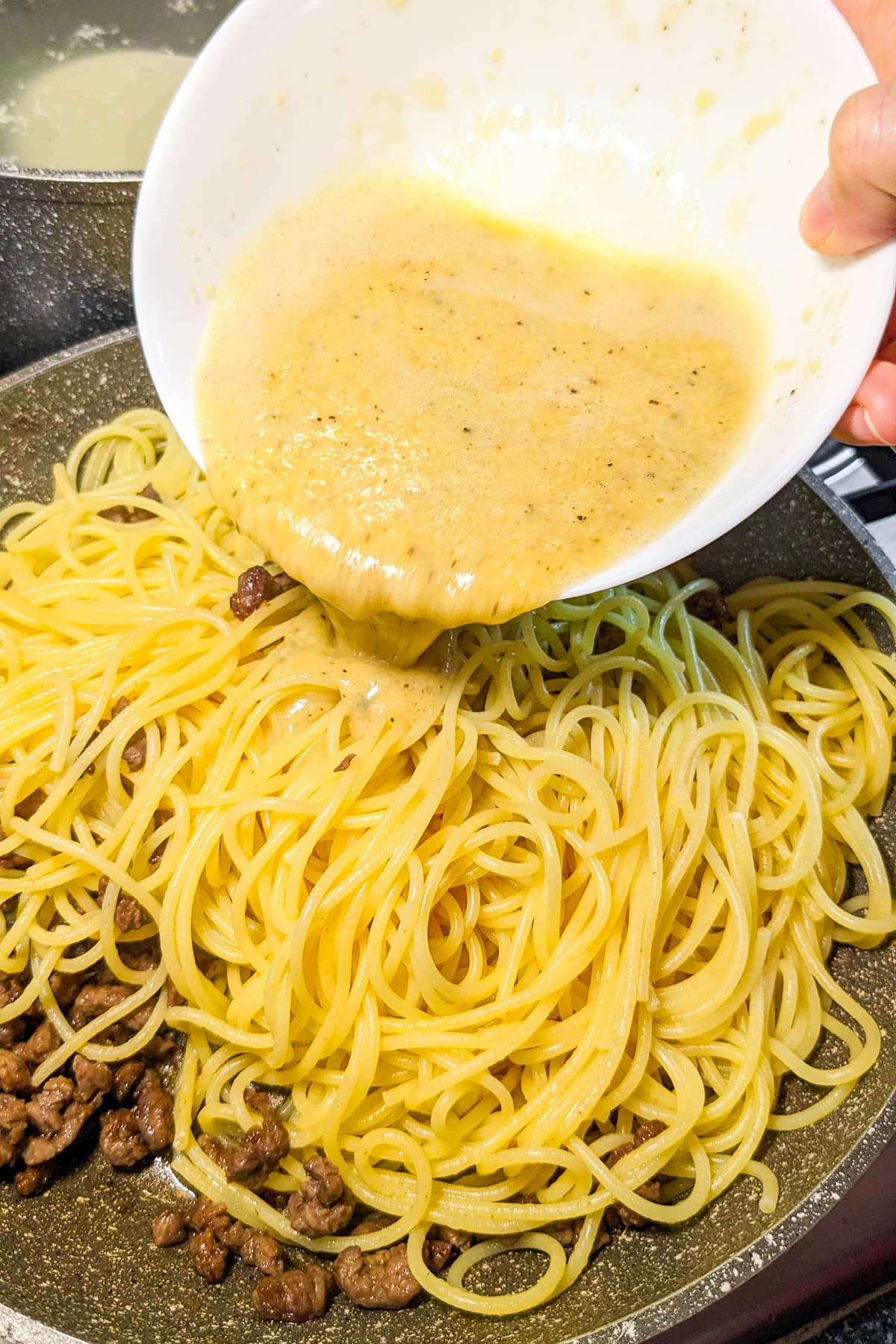 Pouring egg-parmesan sauce over beef and spaghetti.
