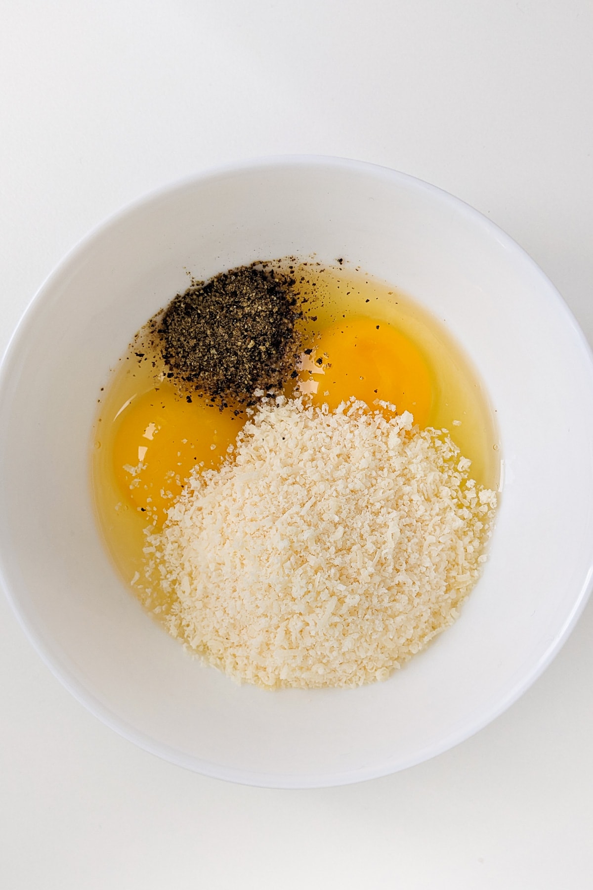 Top view of two raw eggs with black pepper and parmesan cheese.